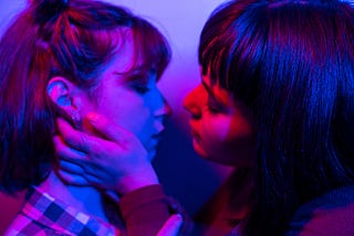 two young women in an embrace under blue light