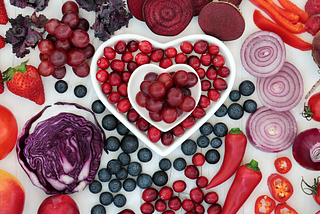 Blue, red and purple fruits and vegetables arranged into art forming a heart.