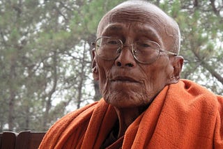 Picture of an old Buddhist monk with weathered face and an orange robe draped over his shoulder