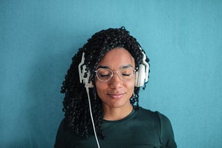 Headshot of a woman with long curly hair against a blue background smiling as she listens through headphones.
