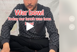 A paused video of a man (Hamada Shoo) sitting in front of a cutting board captioned “War bowl Today our lunch was tuna bowl” in front of a tarplike material