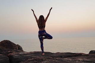 Woman in yoga pose on one leg facing a sunset