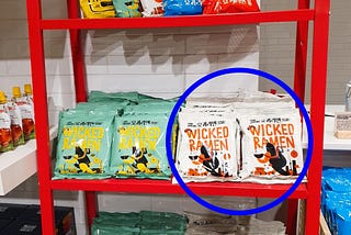 A blue circle pointing out the Wicked Ramen (Yogoe Ramyeon) Itaeweon Chamggae Majemat packages on a shelf.