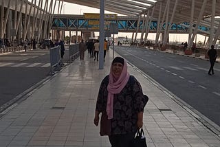 The blogger wearing grey joggers, a black and pink floral top and pink hijab standing outside the arrival hall at Cairo International Airport