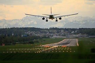 A passenger plane landing on a runaway with the Swiss Alps in the distance. It’s either sunrise or sunset.