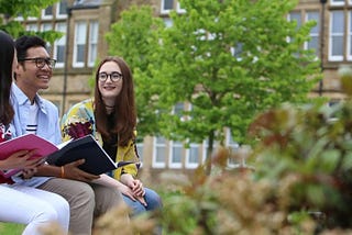 three students sitting on a wall chatting