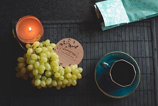 Image of a cup with grapes, a candle, and black tea spilling from a bag.