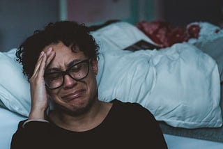 A woman crying on the side of her bed.