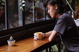 woman sitting alone at a table, drinking coffee