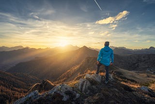 A man on a rocky hill with  beautiful mountains at sunset before him. Dolomites, Italy.