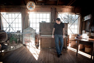 Gentry Bronson standing in front of an upright piano in Tomales Bay, California