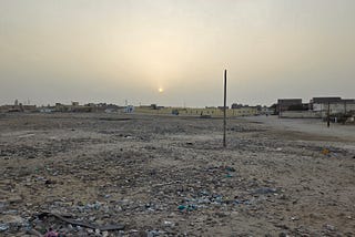 Hazy sunset above an empty lot with trash strewn about