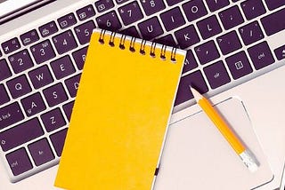 Otwarty laptop, ołówek, telefon i notes na klawiaturze. Obraz przedstawia temat — gdzie szukać pracy zdalnej?
