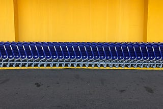 A row of blue shopping carts in front of a yellow wall.