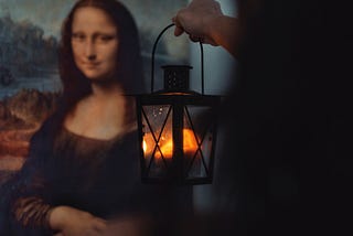 A hand holding a lantern in front of Da Vinci’s Mona Lisa painting.