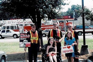 Two young women with three firefighters in front of fire truck.