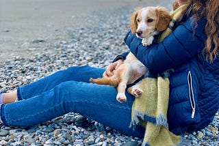 girl sitting on the beach with her dog in her arms