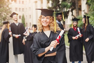 Blonde woman holds diploma. Wears grad attire.