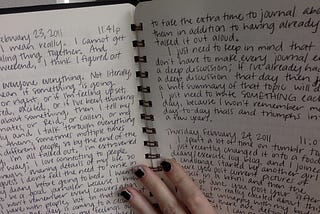 a hand holding up a spiral notebook open to a spread of journaling on both pages
