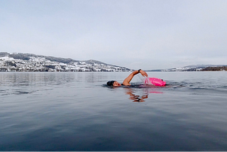 Female swimming front crawl in lake with snow on the surrounding hills.