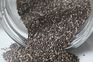 Dry chia seeds tumbling out of a small glass far onto a countertop. Photo by Delphine Hourlay: https://www.pexels.com/photo/fish-food-inside-jar-691162/