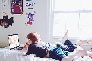 Brothers laying on a bed watching a laptop.