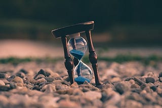 A small hourglass standing amidst pebbles.
