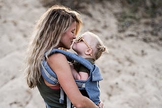 A mother carrying and kissing her toddler daughter