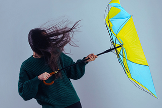 Woman trying to hold onto a broken umbrella in wind.