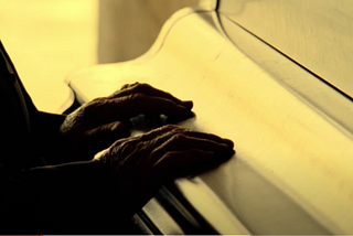 Hands at the piano, the keyboard cover closed.