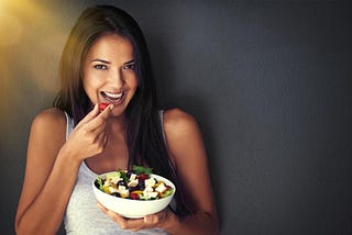 Portrait of a healthy young woman eating a salad against a gray background.