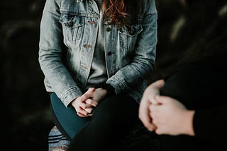 Photo of a woman in the background, head obscured by the top of the frame, and an individual foreground, likely counselling.