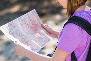 Young woman with a baseball cap peering down at a map