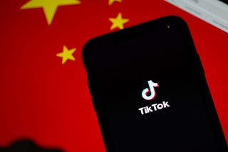 A phone displaying the TikTok logo is placed in front of a Chinese flag.