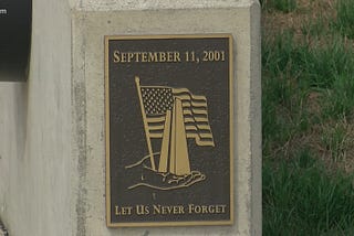 September 11 memorial with a flag, the date of the attack and the words, “Let Us Never Forget”