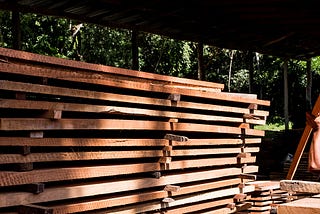 A worker lifts a piece of wood onto a  tall stack of lumber sitting underneath a metal-roofed shelter in an FSC-certified forest in Guatemala.