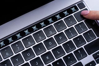 A closeup image of an Apple keyboard with a Touch Bar, and the touch bar features a row of skulls