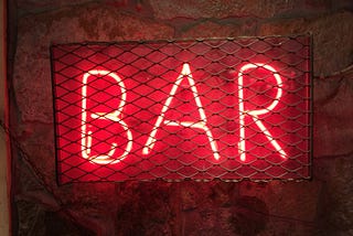 Red neon sign that says bar under some chain metal