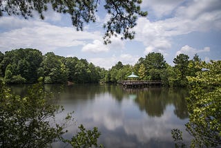 A beautiful, tranquil photo of a body of water surrounded by green trees, with a blue sky overhead that’s reflected in the water.