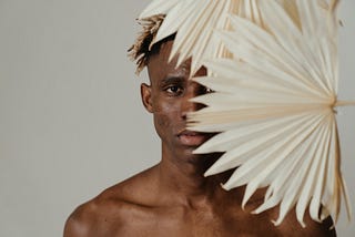 A person of color on white dreadlocks, standing behind a flower