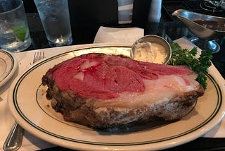 A slab of rare prime rib on a plate, with a small ramekin of horseradish sauce and a parsley garnish.