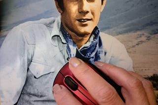 A female hand using a red computer mouse rests on a mouse pad featuring good-looking, dark haired actor Robert Fuller from the 1959–1963 TV western Laramie.