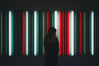 A person standing in front of several vertically hung flourecent lights in a darkly lit room