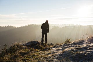 Solo Travel — Man standing atop a hill overlooking the landscape (https://unsplash.com/@capturethemoment)