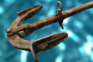 Old, rusty, ornate anchor on a blue water background.