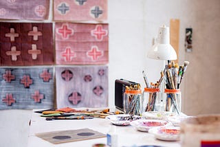 A wall covered in hand-drawn patterned paintings with a table nearby holding paintbrushes in cups. It hints at a creative and decorative setting.