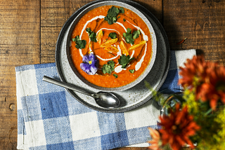 A bowl of soup sitting upon a napkin with flowers nearby