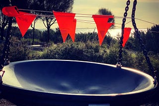 Red flags mark prohibited entry to a playground. A large bowl swing hangs from chains.