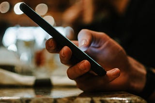 Hand typing on a smartphone in a dimly lit bar or restaurant.