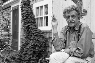 Kurt Vonnegut fumando à direita, ao lado de uma porta e uma trepadeira